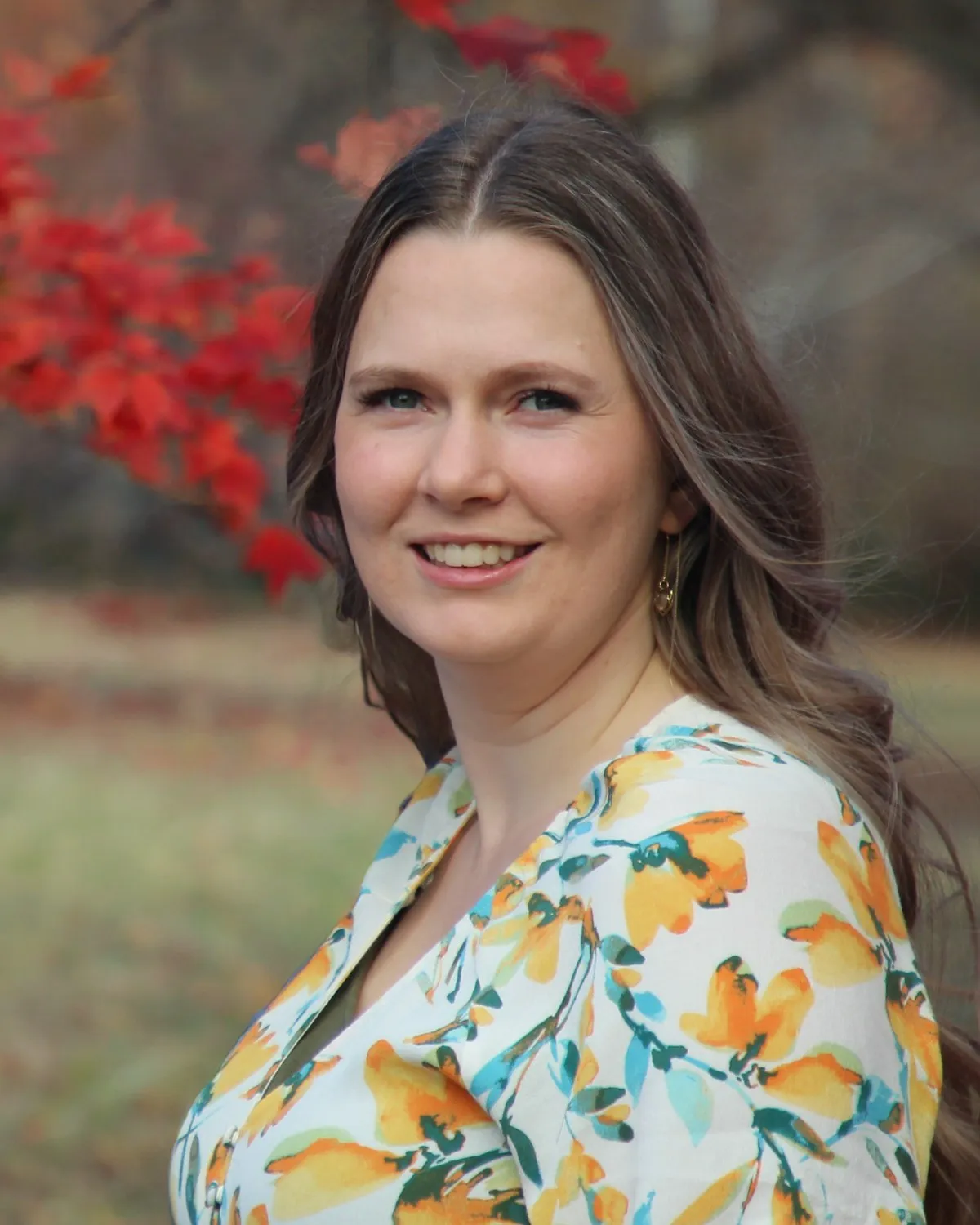 Portrait of Autumn Clark, smiling, with red autumn leaves behind her.